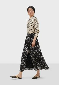Blusa a pois beige e neri; abbinata a una gonna nera fluida con pois beige, dotata di uno spacco frontale. Indossata con mule nere con perline.