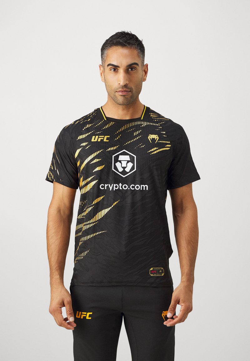 Crna atletska majica s zlatnim naglascima, s teksturiranim dizajnom, UFC logotipom i središnjim grafičkim prikazom s natpisom "crypto.com."