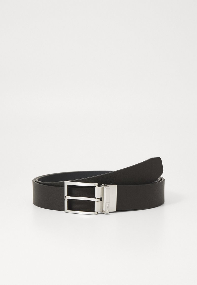 Ceinture en cuir noir avec une boucle en argent poli. La sangle est plate et lisse, présentant une texture subtile et une extrémité arrondie.