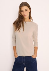Beige long-sleeve top with a rounded neckline, smooth texture, and relaxed fit, paired with dark blue denim jeans featuring visible stitching.