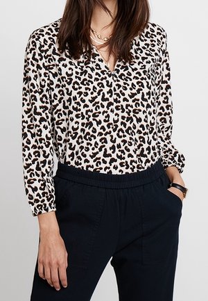 Halenka s leopardím vzorem, výstřihem do V, dlouhými rukávy a elastickými manžetami. Vzor obsahuje černé a hnědé skvrny na krémovém pozadí. Kombinováno s tmavými kalhotami.