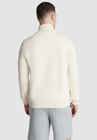 Light cream pullover with a high collar and long sleeves. Soft texture, ribbed cuff details, and a relaxed fit. Paired with gray shorts.