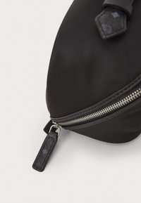 Sac en tissu noir avec une fermeture éclair argentée brillante, de forme ovale, tirette de fermeture éclair texturée et surface lisse. Pas de motifs ou d'accents visibles.