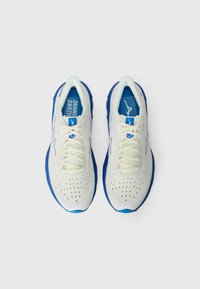 Baskets de course en crème clair avec des accents bleus, tige en mesh, fermeture à lacets, col rembourré et détails perforés pour la respirabilité.