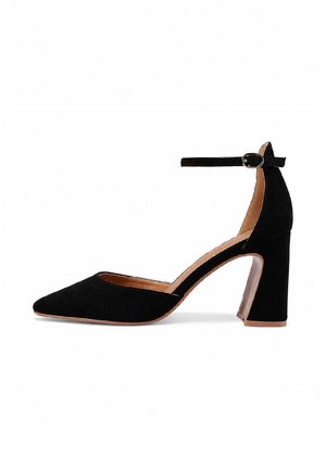 Scarpa con tacco alto in camoscio nero con punta affilata, cinturino alla caviglia con fibbia, tacco a blocco e fodera interna color marrone chiaro su sfondo bianco.