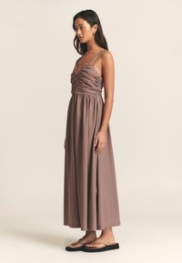 Maxi-kjole i mauve stof med justerbare dobbelte stropper, rynket overdel og flydende nederdel. Kombineret med minimalistiske flade sandaler.