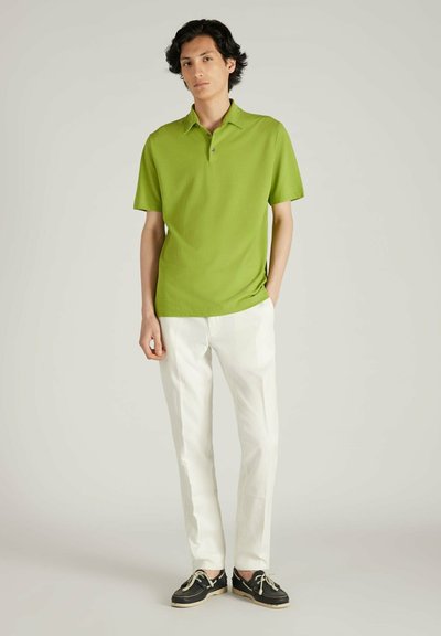 Polo verde con mangas cortas, un cuello y dos botones, combinado con pantalones de lino blancos y zapatos de barco negros. Diseño simple y limpio.