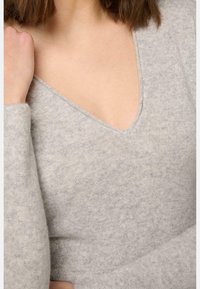 Pull léger gris clair avec un décolleté en V profond, texture douce, manches longues ajustées et un motif de tricot lisse et homogène.