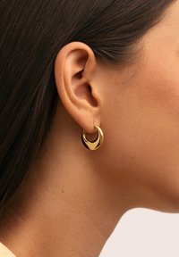 Orecchini a cerchio in oro caratterizzati da una finitura lucida e elegante con una forma a mezzaluna. Il design incorpora curve morbide e una texture lucida.