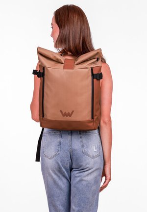 Batoh s rolovaným vrchem v béžové tkanině s hnědými akcenty, nastavitelné popruhy a boční zipy. Na přední straně se nachází nášivka s logem.