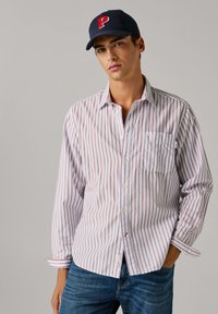 Valge triibuline nööpidega särk peente punaste joontega, millel on rinnatasku ja nööpidega varrukaservad, kombineeritud siniste teksade ja mereväe sinise barettmütsiga.