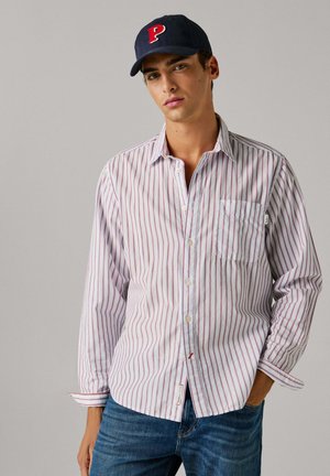 Valge triibuline nööpidega särk peente punaste joontega, millel on rinnatasku ja nööpidega varrukaservad, kombineeritud siniste teksade ja mereväe sinise barettmütsiga.