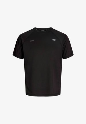 Garçon blond debout et souriant, portant un t-shirt de sport noir à manches courtes, un short noir, des chaussettes blanches avec des rayures noires et des baskets blanches.