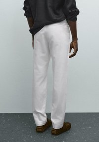 Weiße, maßgeschneiderte Hose mit geradem Schnitt, aus glattem Stoff. Getragen mit braunen Slippern. Ansicht von hinten, die Taschen und nähtechnische Details zeigt.