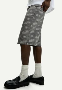 Denim shorts in gray with a repeated "digital" logo pattern. Features a straight cut and standard pockets. Paired with black loafers and white socks.