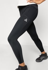 Μαύρο αθλητικό κολάν με εφαρμοστή σχεδίαση, που διαθέτει λογότυπο, αντίθετη ραφή και πλευρικές τσέπες για αποθήκευση.