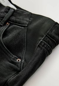 Tessuto di denim nero con una finitura testurizzata, dotato di una vita e un pannello a maglia a contrasto. Include dettagli in metallo con bottoni.