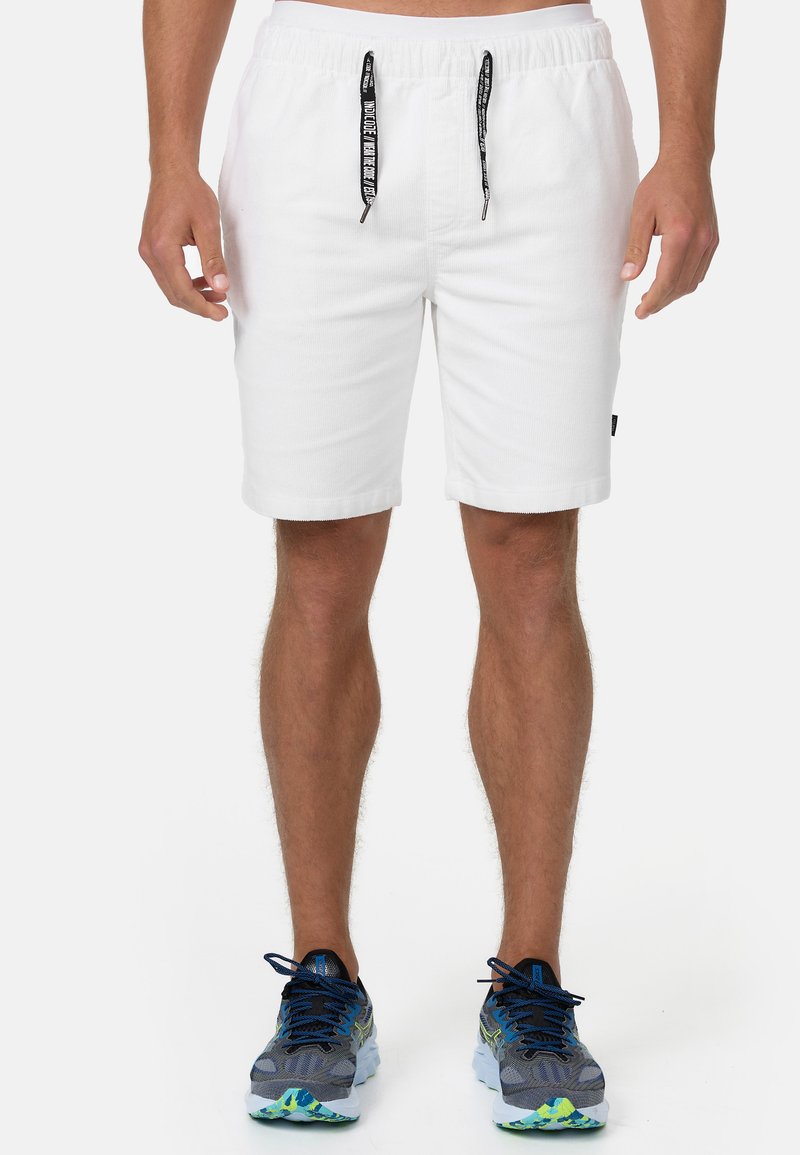 Witte katoenen shorts met een elastische tailleband en zwarte trekkoordjes. Beschikt over zijzakken en heeft een ontspannen pasvorm, weergegeven met sportieve schoenen.
