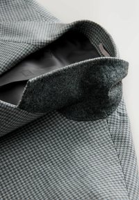 Textured gray blazer with a houndstooth pattern. Features a soft felt inner collar and smooth black lining. Tailored design with precise stitching.