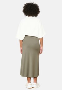 A loose white sweatshirt with a wide neckline paired with a long olive green skirt. Model wears white sneakers, showing a casual outfit.