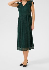 Grön knälång klänning av texturerat tyg med diamantmönster, V-ringning och volangärmar. Har en genomskinlig spetskant nederst.