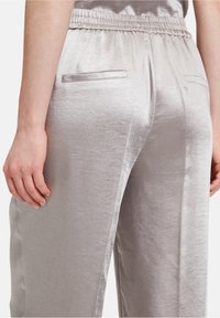 Ljusgrå satintrogger med elastisk midja, sidofickor och en slät, glansig yta. Har en strömlinjeformad silhuett.