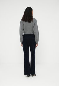 Szürke, hosszú ujjú felső, bordázott textúrával, sötétkék kordbársony, harangszárú nadrággal párosítva. A modell hátulról áll, fekete magassarkú cipőt visel.