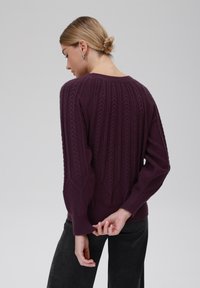 Pflaumenfarbener Strickpullover mit strukturierten Mustern und gerippten Bündchen. Verfügt über einen weiten Ausschnitt und eine lässige Passform, kombiniert mit Dunkel und eng anliegenden Hosen.