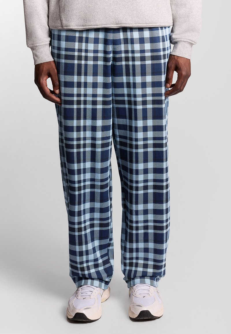 Pantalons de lounge à carreaux en bleu et marine, offrant une coupe décontractée et un tissu doux. Associés à des chaussures de sport de couleur claire.