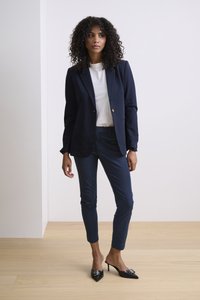Marineblazer mit taillierter Passform und zwei Knöpfen, kombiniert mit passenden schmalen Hosen und spitzen schwarzen High Heels mit einem dekorativen Akzent.