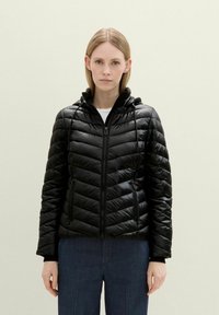 Chaqueta puff negra con un diseño ajustado, puños acanalados, cierre frontal con cremallera y capucha ajustable. Presenta un patrón en forma de chevrón para añadir textura.