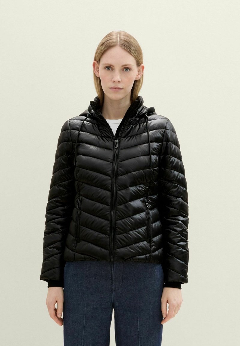 Chaqueta puff negra con un diseño ajustado, puños acanalados, cierre frontal con cremallera y capucha ajustable. Presenta un patrón en forma de chevrón para añadir textura.