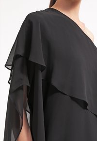 Czarna sukienka z lejącego materiału, z warstwowymi, falbaniastymi rękawami i asymetrycznym dekoltem, o gładkiej teksturze.