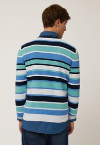 Maglietta polo lavorata a maglia con righe verticali in varie tonalità di blu e verde. Texture a coste, colletto a contrasto e strato di camicia di jeans sotto.