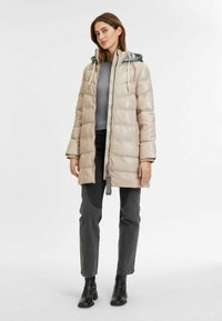Giacca puffer beige con cappuccio grigio rimovibile, chiusura a zip, texture trapuntata e tasche. Abbinala a jeans scuri e stivaletti.