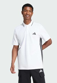 Witte poloshirt met zwarte accenten, korte mouwen en een kraag met twee knopen. Heeft een zwart gestreept ontwerp aan de zijkanten en een Adidas-logo.
