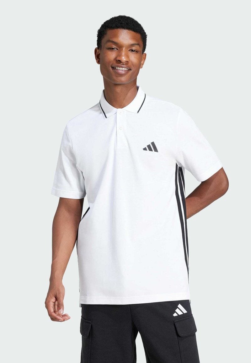Witte poloshirt met zwarte accenten, korte mouwen en een kraag met twee knopen. Heeft een zwart gestreept ontwerp aan de zijkanten en een Adidas-logo.