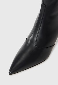 Czarny skórzany botek za kostkę z wydłużonym noskiem, gładką fakturą, minimalnym przeszyciem i eleganckim designem; zamek błyskawiczny po boku dla łatwego zakładania.