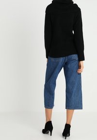 Schwarzer, übergroßer Pullover mit Kapuze, kombiniert mit blauen, cropped Jeans und schwarzen, hohen Stiefeln. Glatte Textur, lässiges Design.