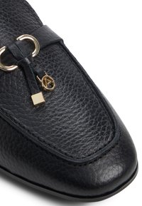 Scarpa in pelle nera con superficie testurizzata. Presenta un accento con fibbia dorata e un piccolo charm quadrato. Punta arrotondata e bordi lisci.