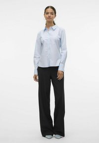 Camisa de manga larga azul claro con botones en el frente y cuello, combinada con pantalones de pierna ancha negros. Tela suave, corte ajustado y diseño nítido.