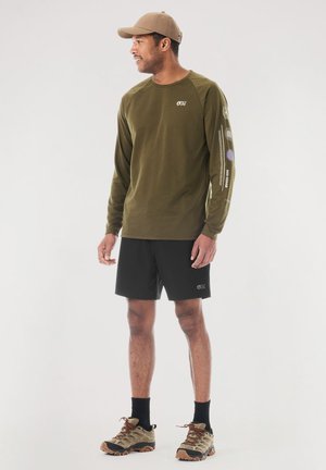 Olive green long-sleeve shirt with logo, black shorts, and beige cap. Shoes are tan with dark accents, suitable for casual or outdoor wear.