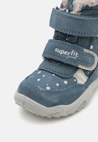 Blaue Kinderstiefel aus Wildleder und Stoff, mit weißen Punkten, zwei Klettverschlussriemen und einer strukturierten grauen Gummisohle.