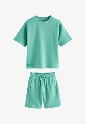 Komplet kratkotrajne teksturirane majice svetlo zelene barve in kratkih hlač z vrvico, priložnostni slog, položen na ravno površino bele podlage.