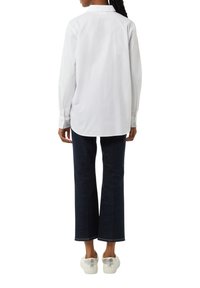 White long-sleeve shirt with a pointed collar, paired with dark blue flared jeans. Footwear features white sneakers with a silver accent.