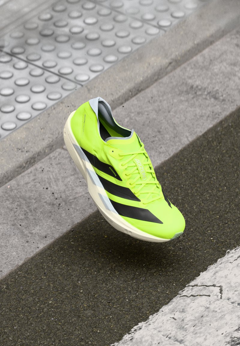 Zapatilla de running de color amarillo brillante con rayas negras, material sintético ligero, suela acolchada y un detalle en gris en el cuello.