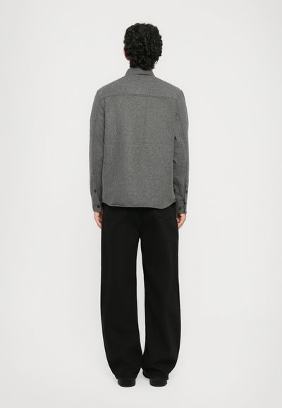 Gray wool shirt with a button-down design, back yoke detail, and cuffed sleeves, paired with loose black trousers. Smooth texture.