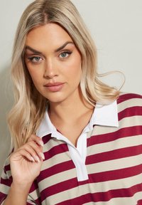 Bordeaux- und beige gestreiftes Poloshirt mit weißem Kragen, aus weichem Stoff und einer Drei-Knopf-Leiste. Schlichtes, lässiges Design.