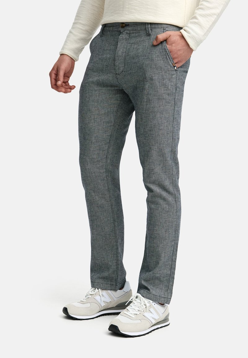 Graue, melierte Hosen mit passgenauem Design, seitlichen Taschen, einem Frontknopfverschluss und einer glatten Textur. Getragen mit weißen Turnschuhen.