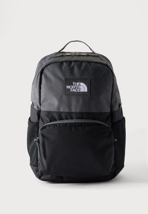 Mochila North Face negra y gris oscuro con bolsillo delantero con cremallera, bolsillos laterales de malla y asa superior sobre un fondo claro.